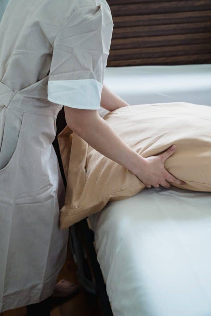 Hotel staff adjusting a pillow on a bed, ensuring guest comfort in a cozy room.